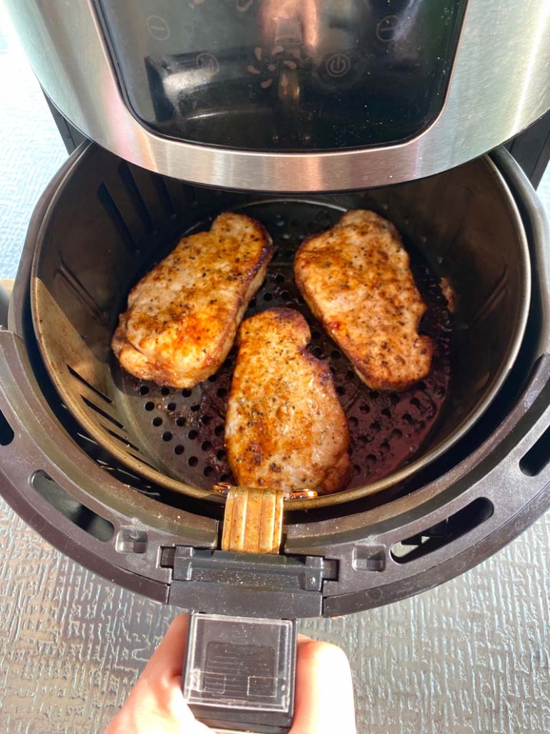 Pulling out the air fryer basket with pork chops inside 