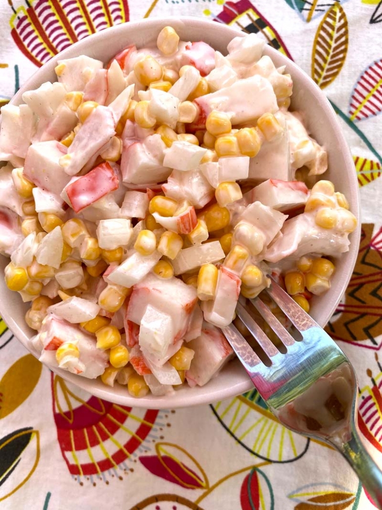 A fork in a bowl of imitation crab and canned corn salad 