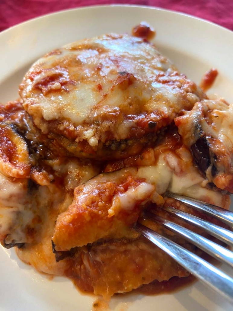 A fork cutting into some baked eggplant parmesan