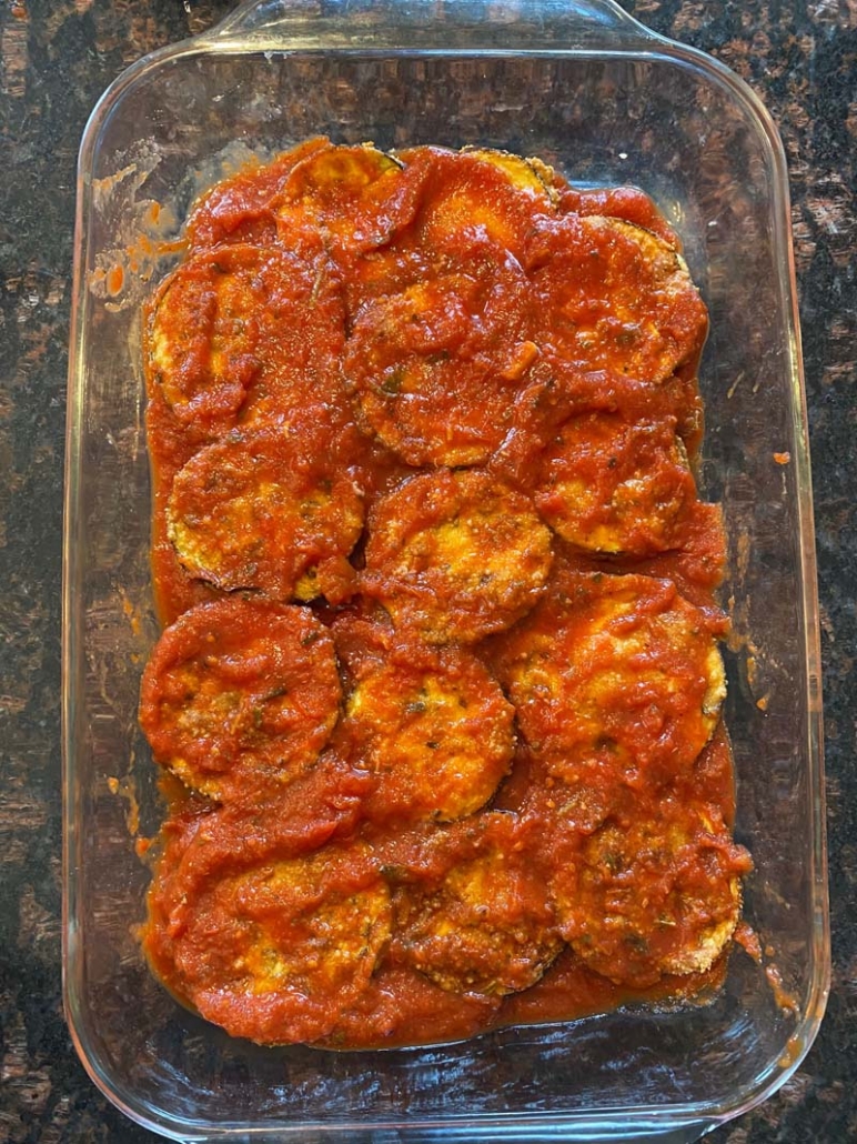 Spreading more marinara sauce on top of baked eggplant