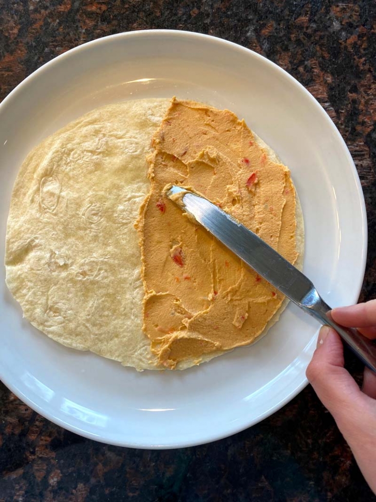 Using a butter knife to spread hummus on a flour tortilla