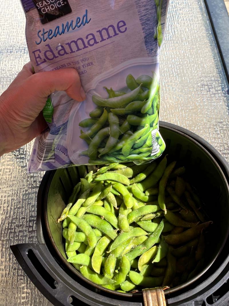 pouring bag of frozen edamame in the air fryer basket 