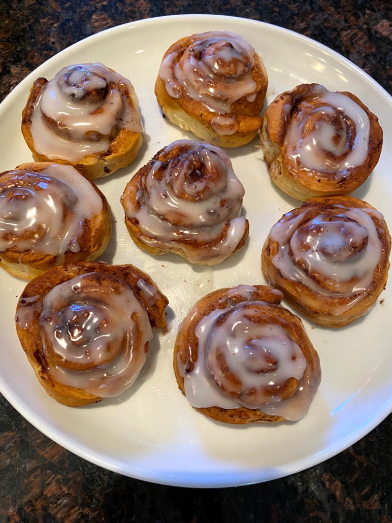 fluffy cinnamon rolls on a white plate with sugar icing 