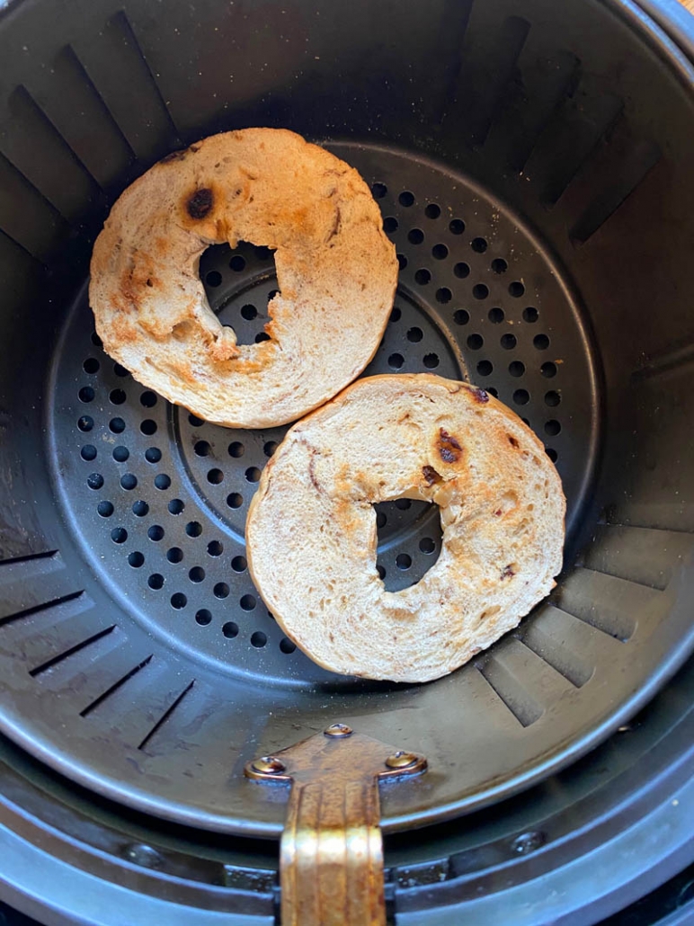 2 halves of a bagel in an air fryer basket 