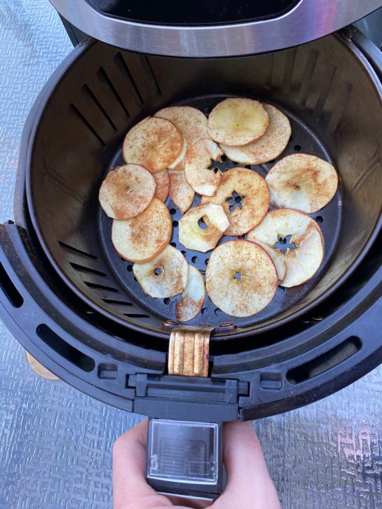 sprinkled cinnamon on apple slices in an air fryer basket