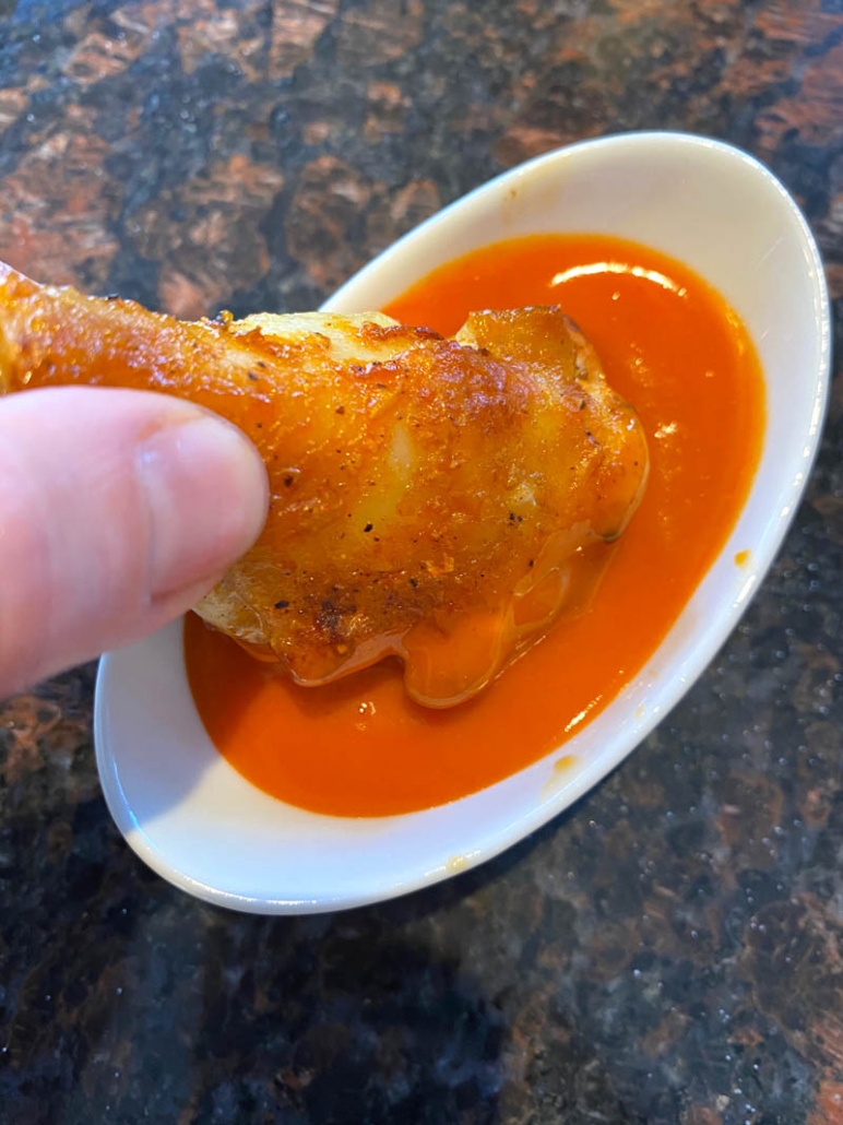 dipping a chicken wing in buffalo sauce 