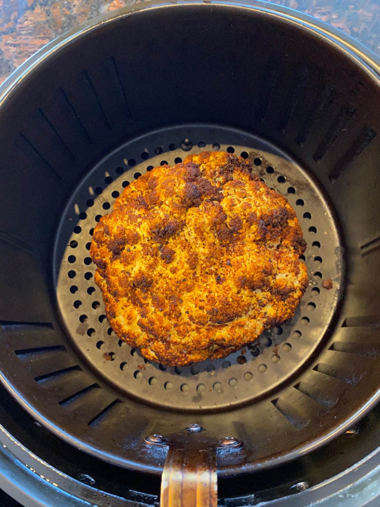 Pulling a roasted cauliflower out of the air fryer 