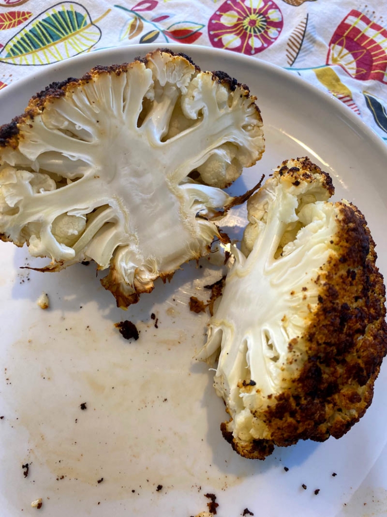 A roasted head of cauliflower cut in half on a white plate 