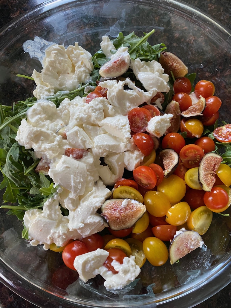 adding all of the ingredients for arugula burrata salad to a bowl 