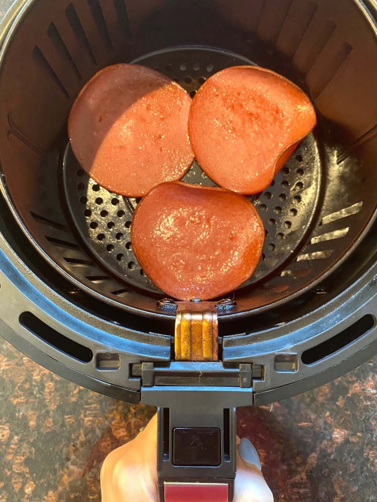 hand holding air fryer basket with bologna