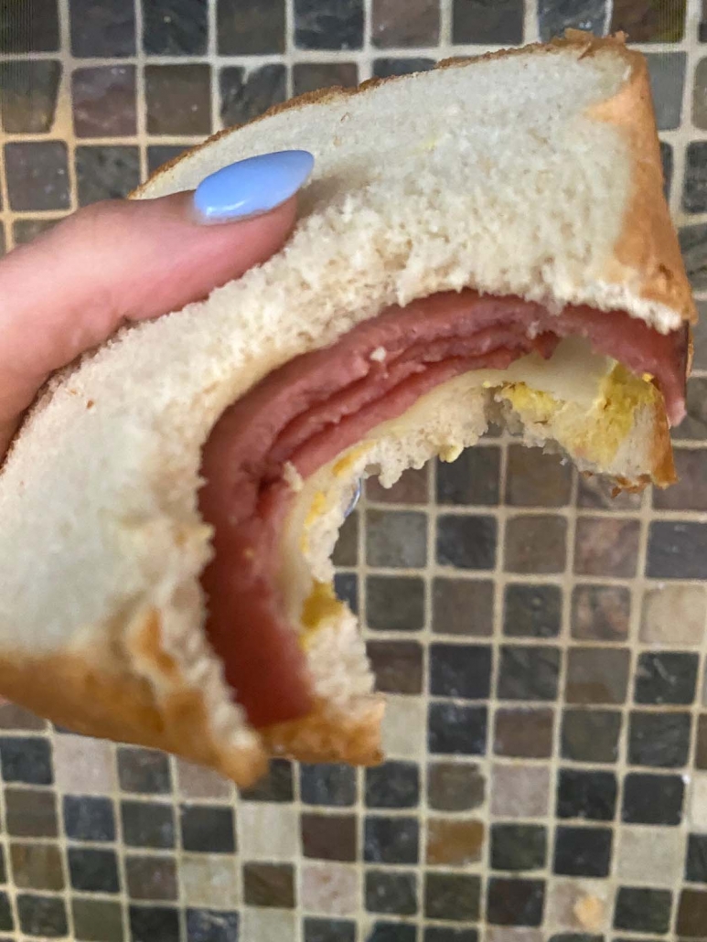 bologna sandwich with bite taken out and held in hand