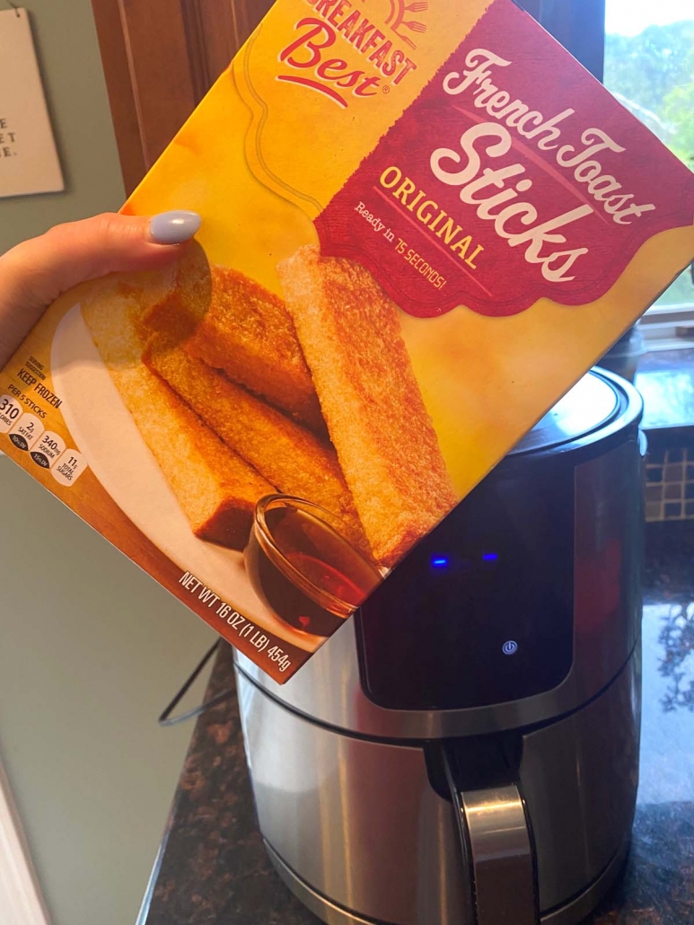 hand holding package of frozen french toast sticks in front of air fryer