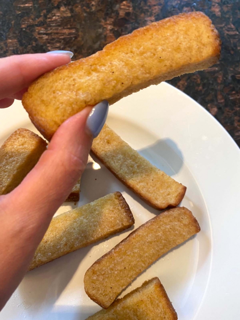 hand holding french toast stick above plate of french toast sticks