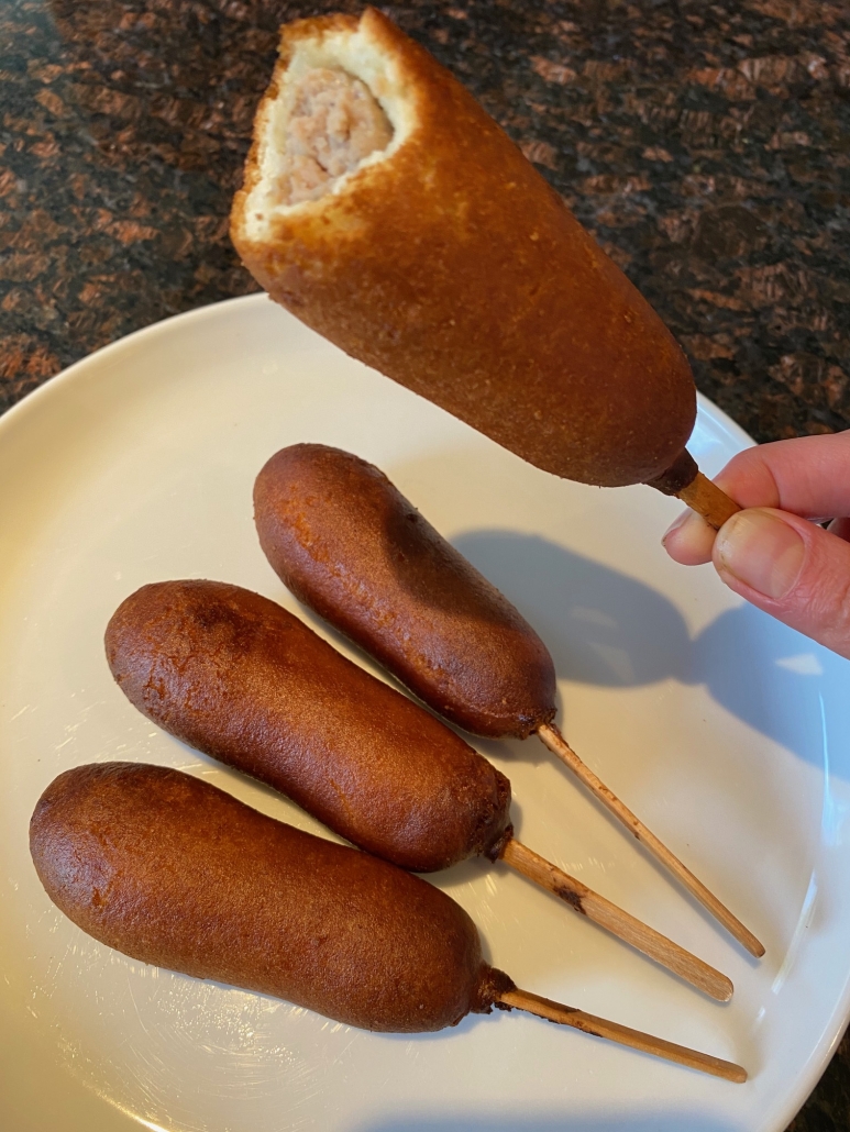 taking a bite out of sausage and pancake on a stick 