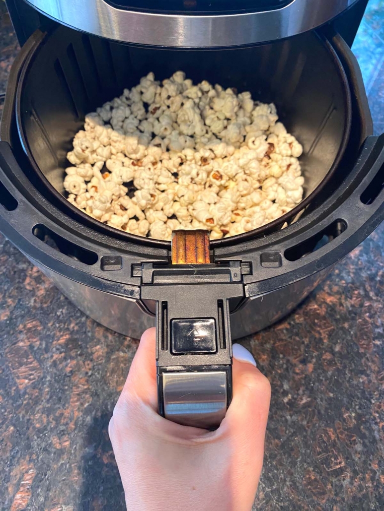 hand holding air fryer basket with popped pop corn