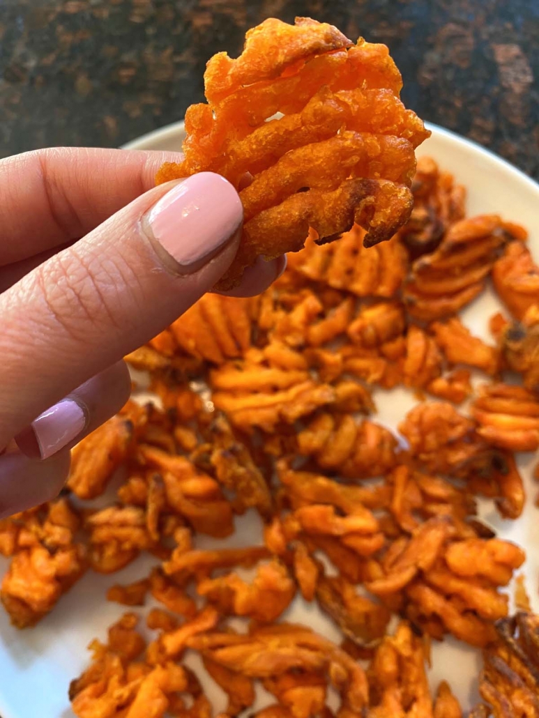 hand holding sweet potato waffle fry over plate of waffle fries