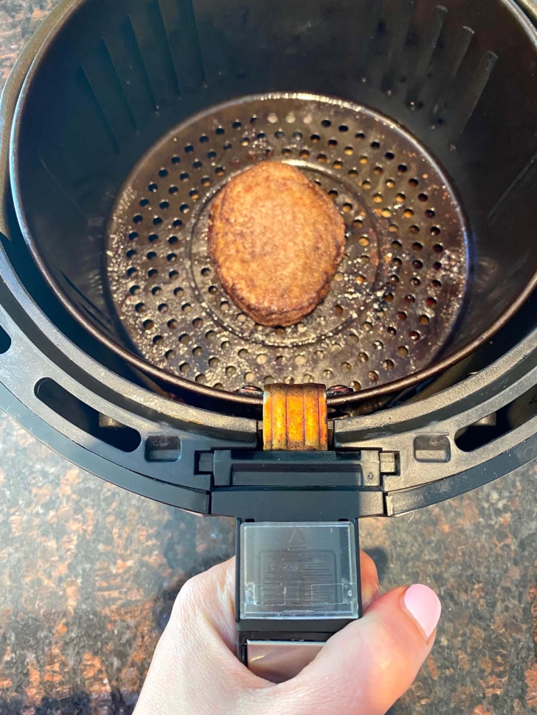 hand holding air fryer basket with turkey burger inside