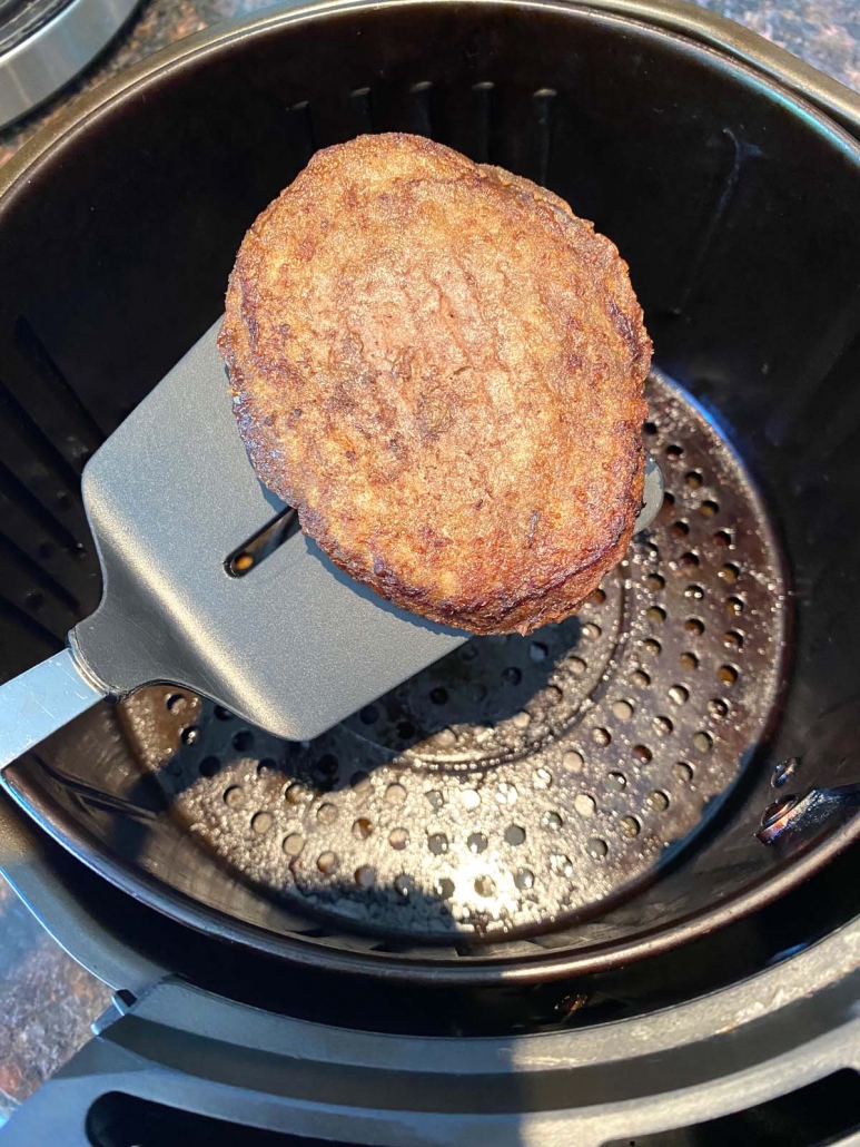 spatula holding cooked turkey burger above air fryer basket