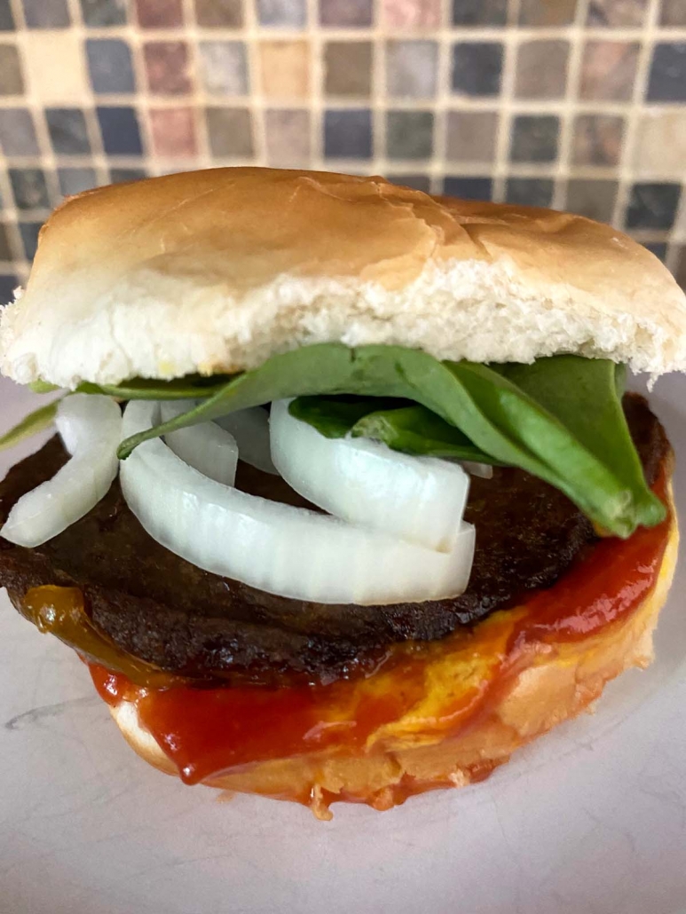 close up of sandwich with lettuce, onion, turkey burger, and ketchup on plate