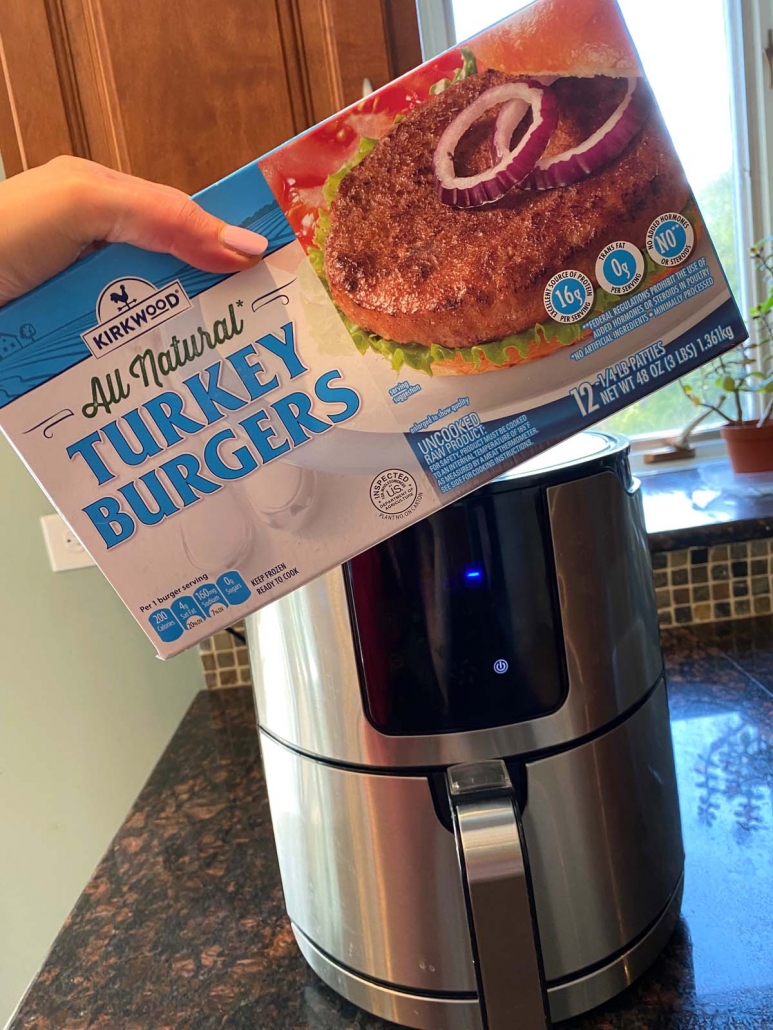 hand holding package of frozen turkey burgers in front of air fryer