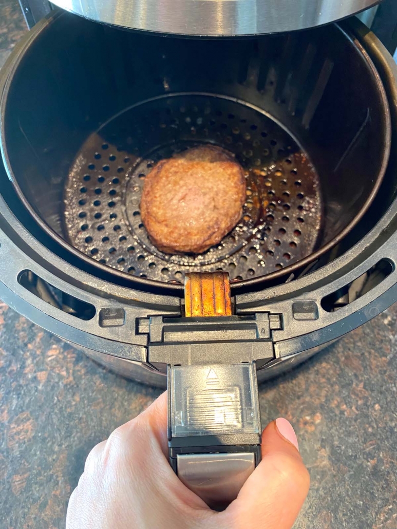 turkey burger cooking in the air fryer with hand holding basket