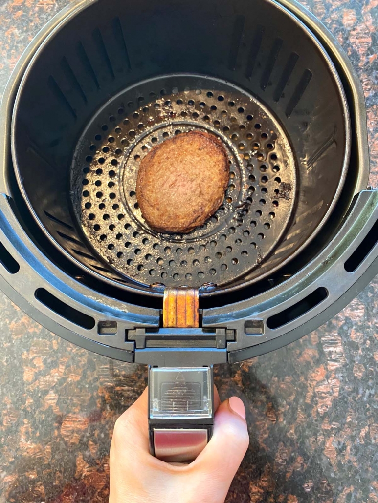 hand holding air fryer basket with cooked turkey burger
