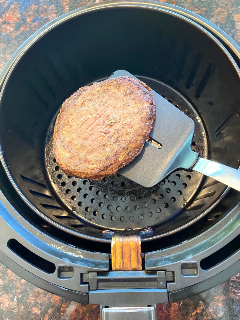 spatula holding a turkey burger above air fryer