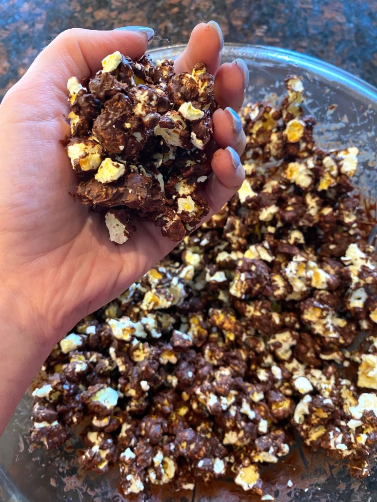 hand holding chocolate covered popcorn above bowl