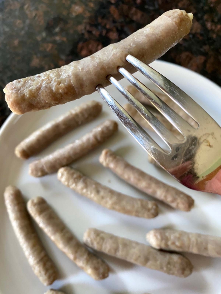 fork holding cooked sausage above plate
