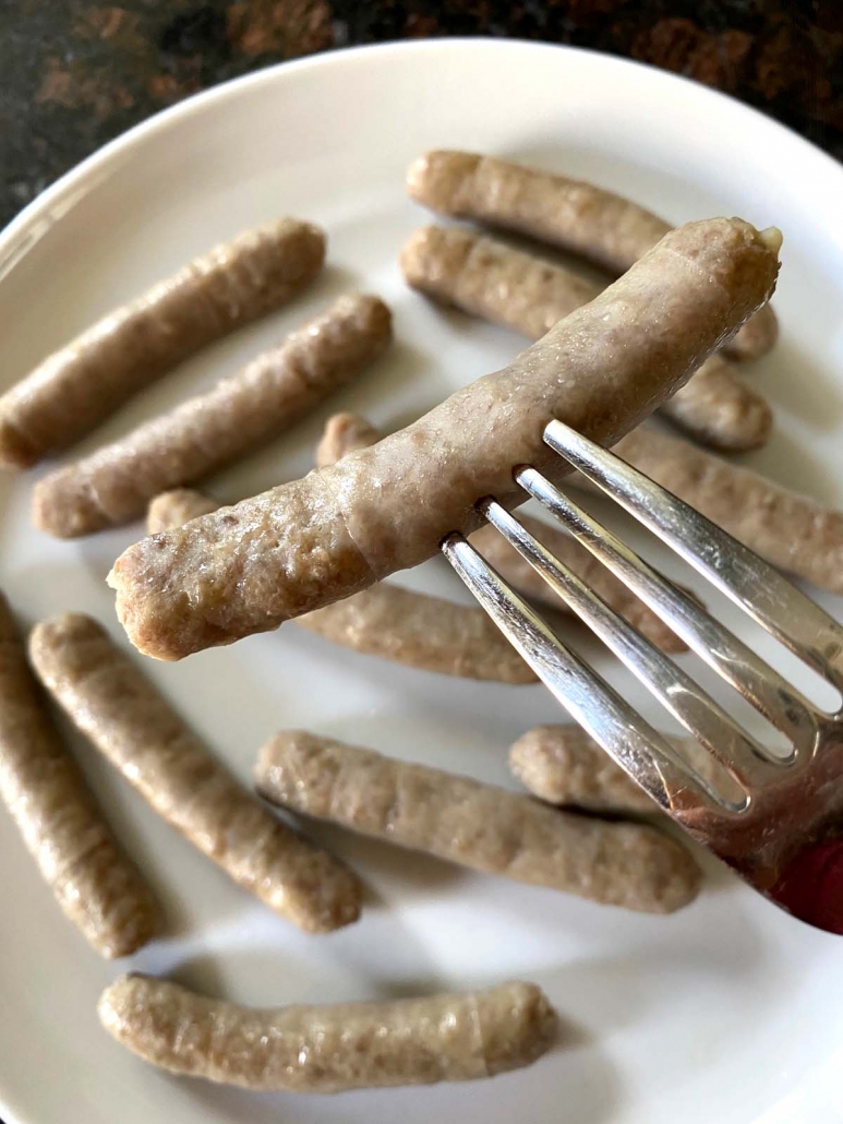 fork holding sausage link above a plate of sausages