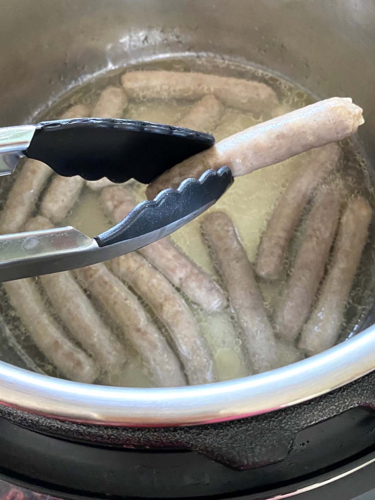 tongs holding sausage link above instant pot