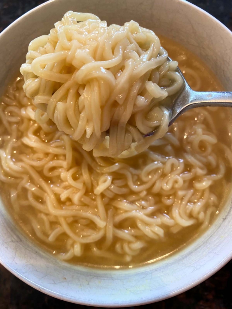spoon holding ramen noodle soup over bowl