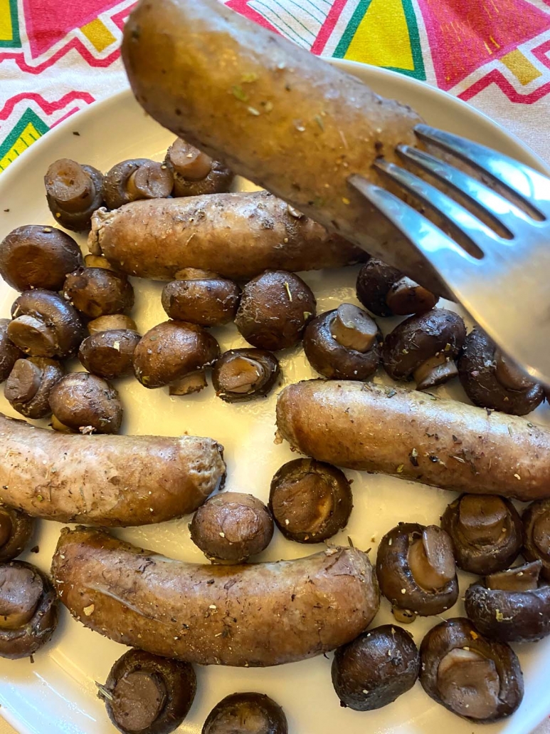 fork holding cooked sausage over plate of mushrooms and sausages