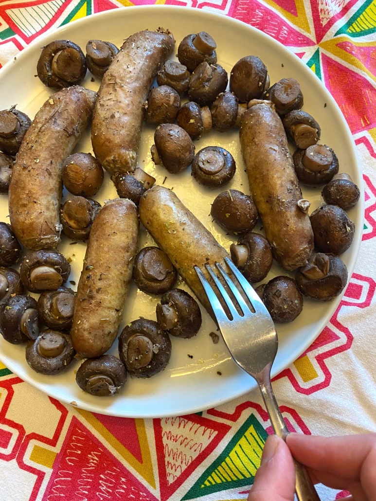 fork stabbing cooked sausage on plate with other sausages and mushrooms