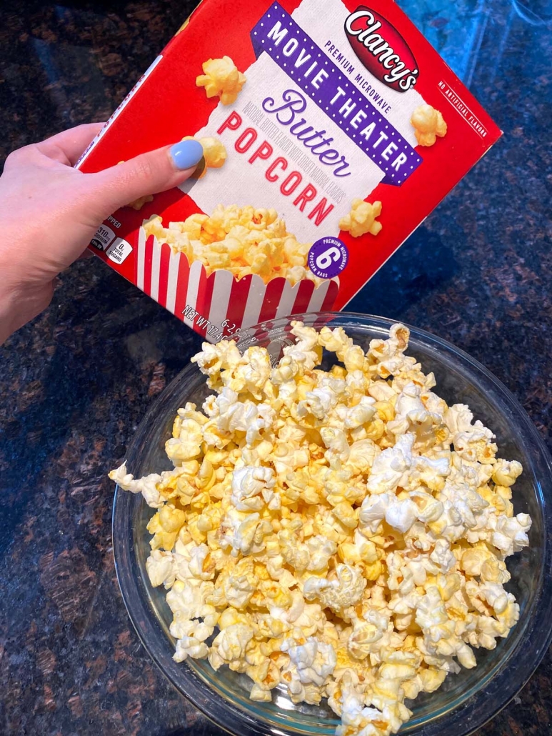 hand holding package of popcorn next to bowl of popped popcorn