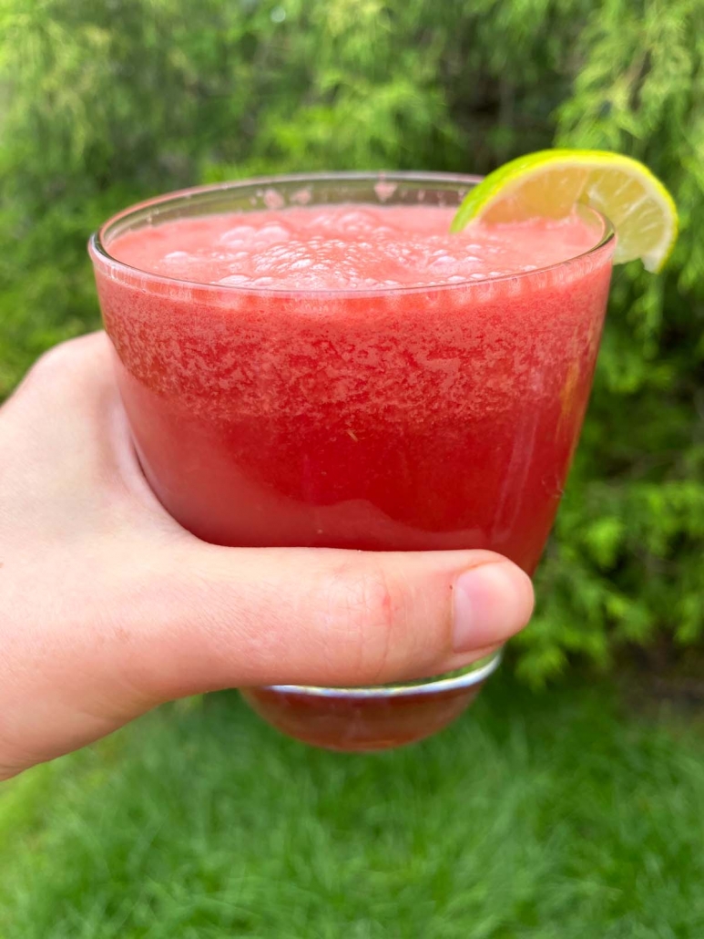 hand holding watermelon smoothie in glass with lime garnish