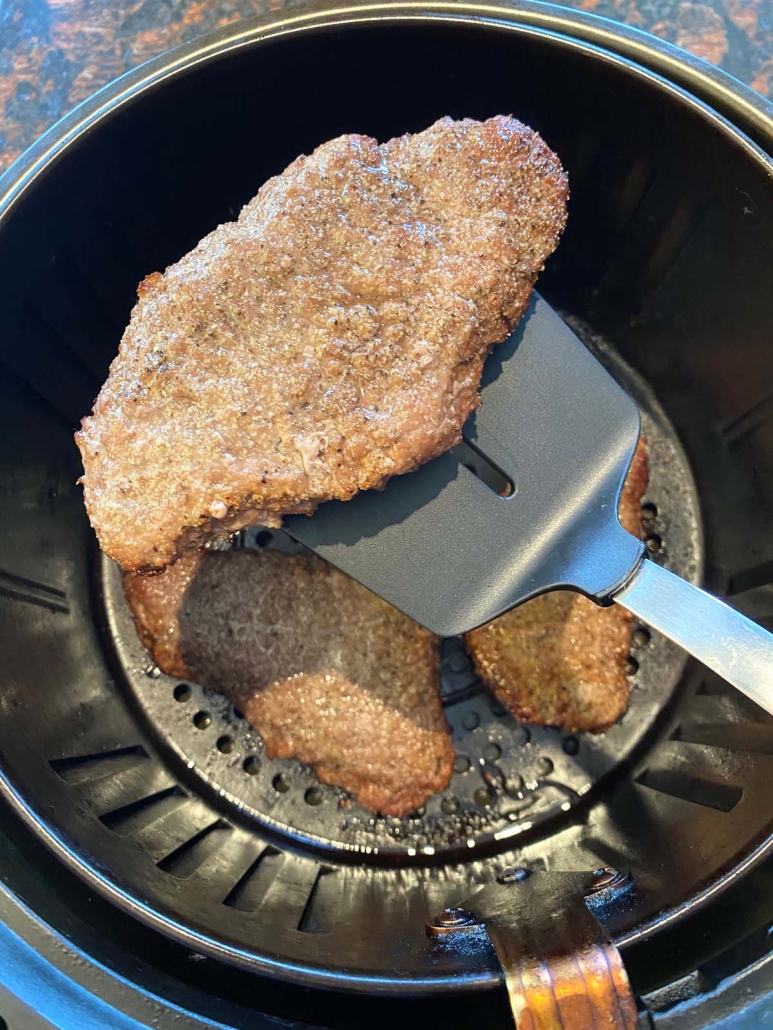 spatula holding 1 cube steak above steaks in the air fryer