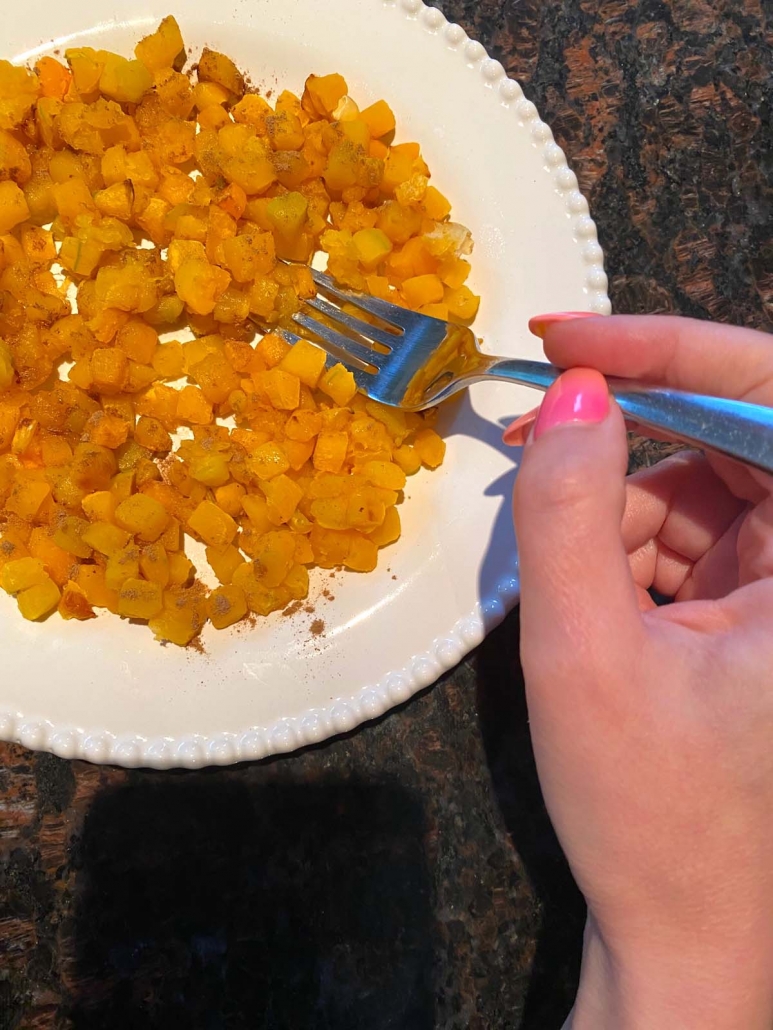 eating air fried butternut squash on a white plate with a fork 