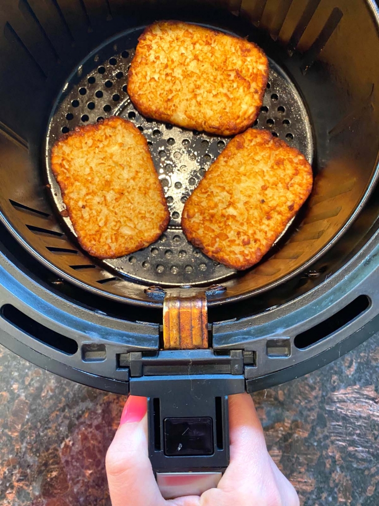 hand holding air fryer basket with hash brown patties inside