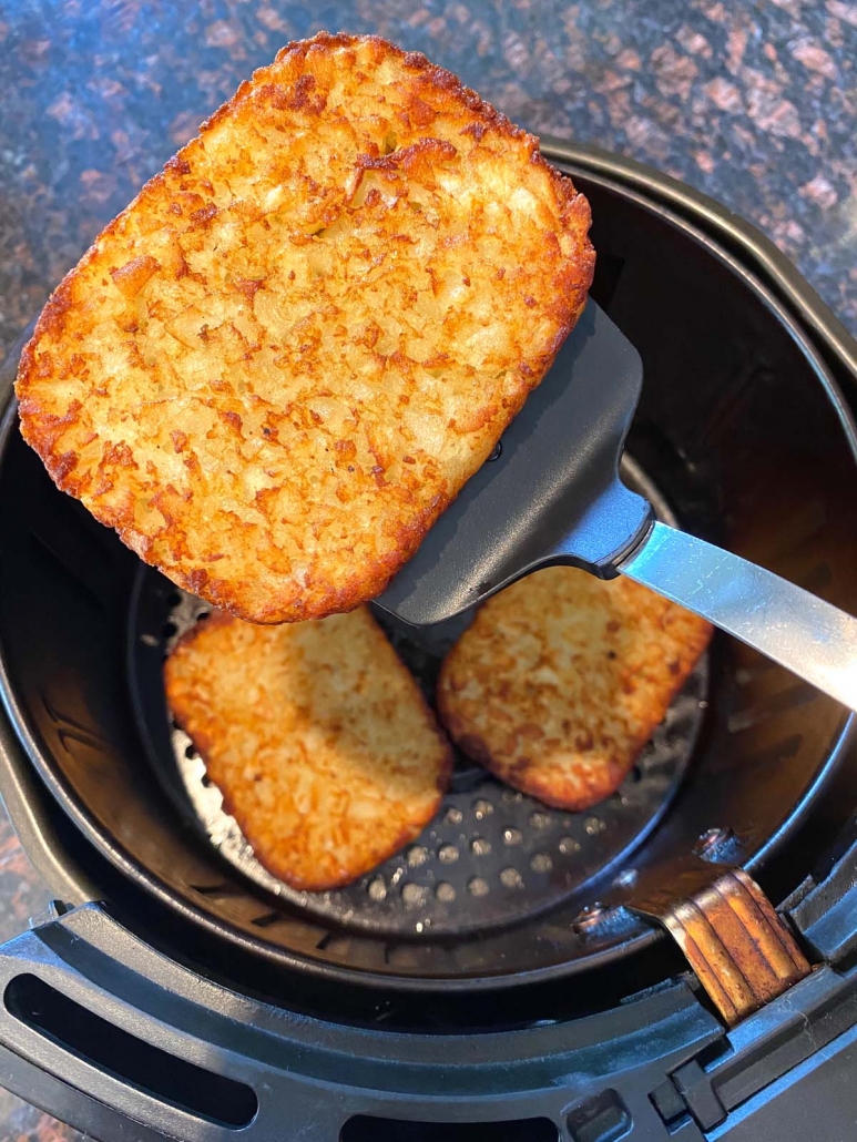 spatula holding cooked hash brown patty over air fryer
