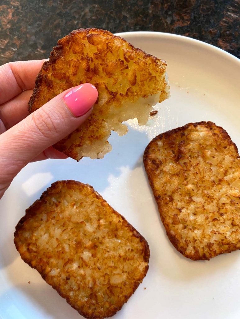 hand holding partial hash brown patty over plate of patties