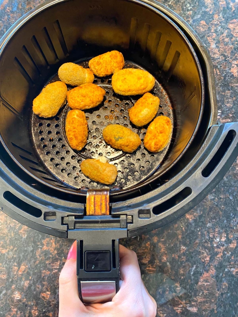 hand holding air fryer basket with frozen jalapeno poppers