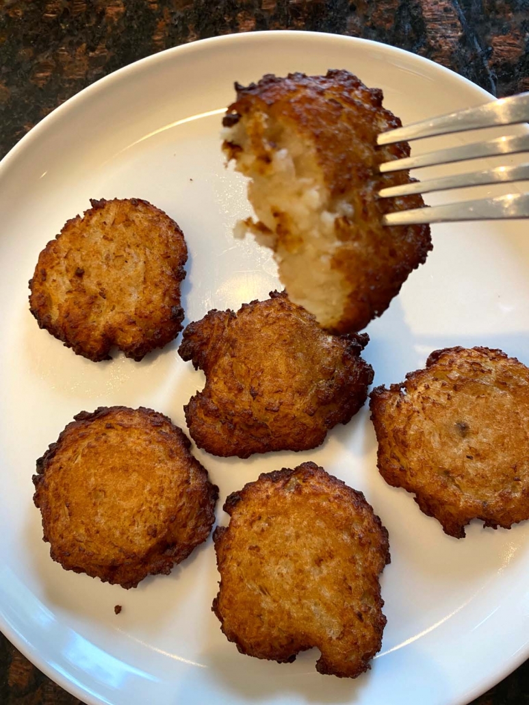 fork holding partial latke above plate of latkes