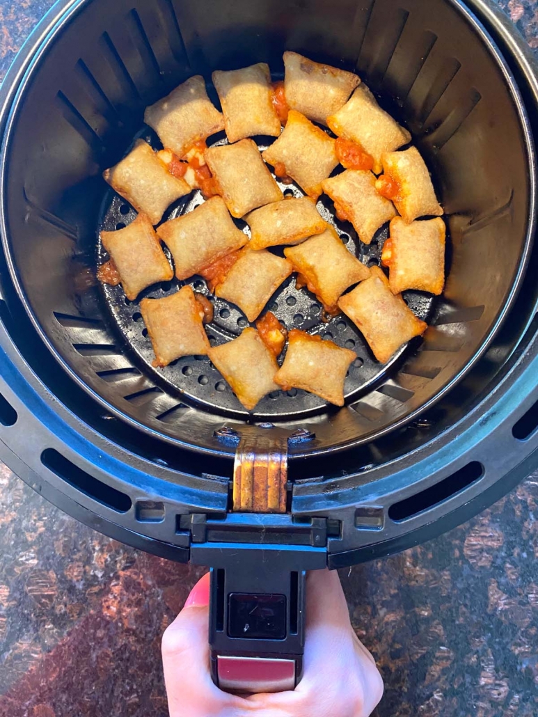 hand holding air fryer basket filled with pizza rolls