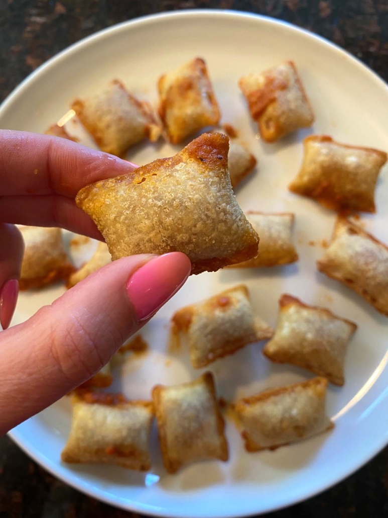 hand holding a pizza roll above plate of pizza rolls