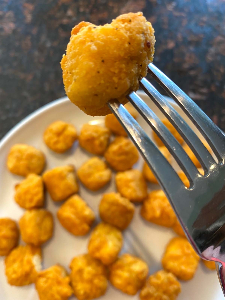 fork holding popcorn chicken above plate filled with popcorn chicken