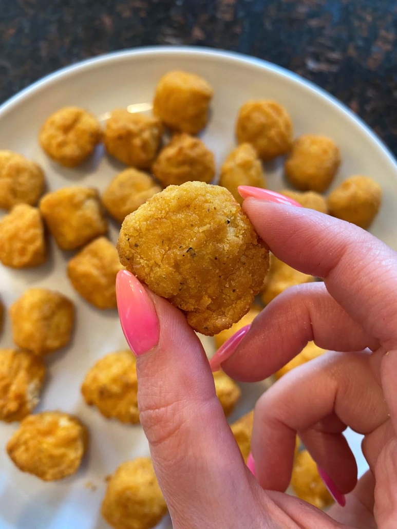hand holding popcorn chicken above plate filled with popcorn chicken