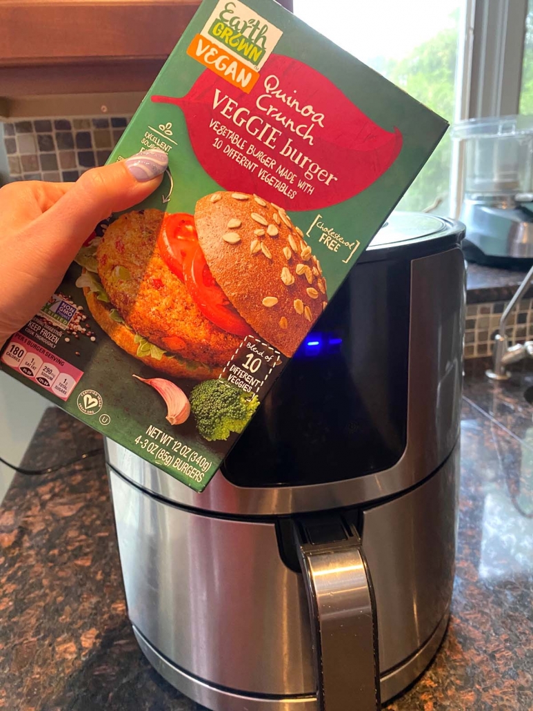hand holding veggie burger box in front of air fryer