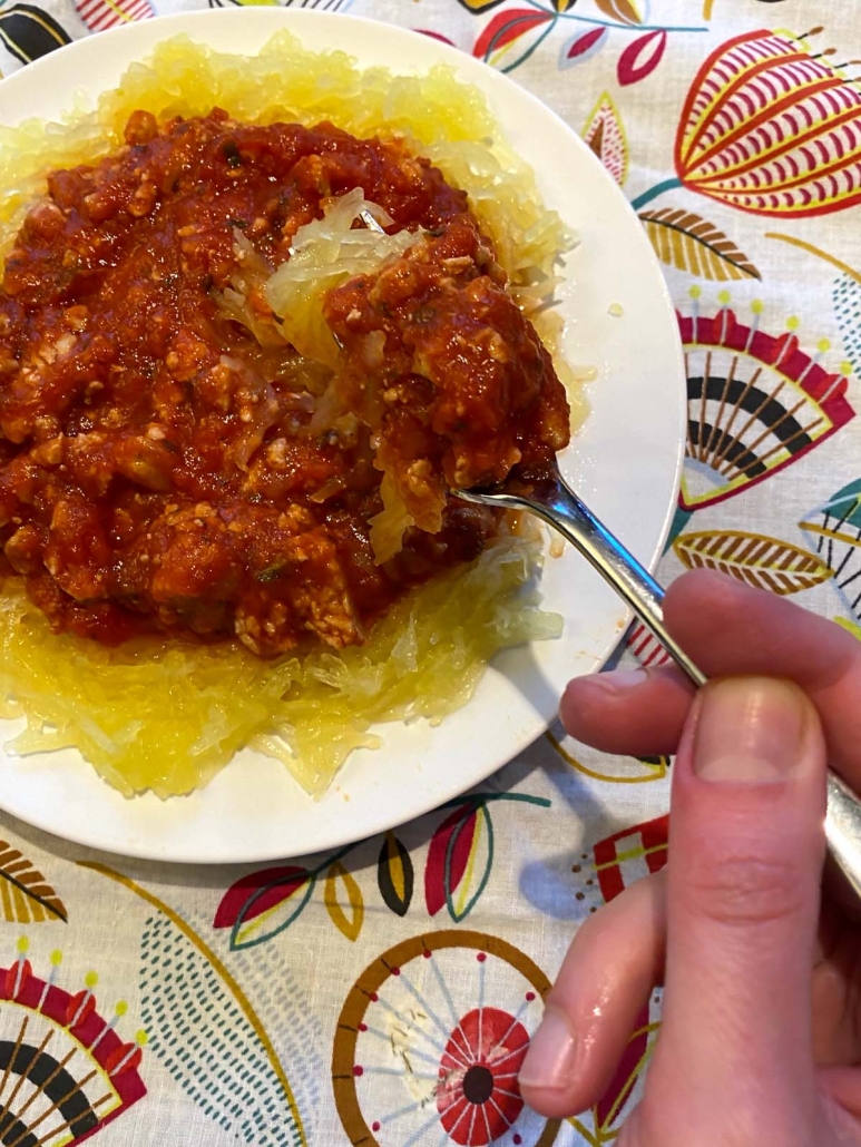 hand holding fork with spaghetti squash and meat sauce