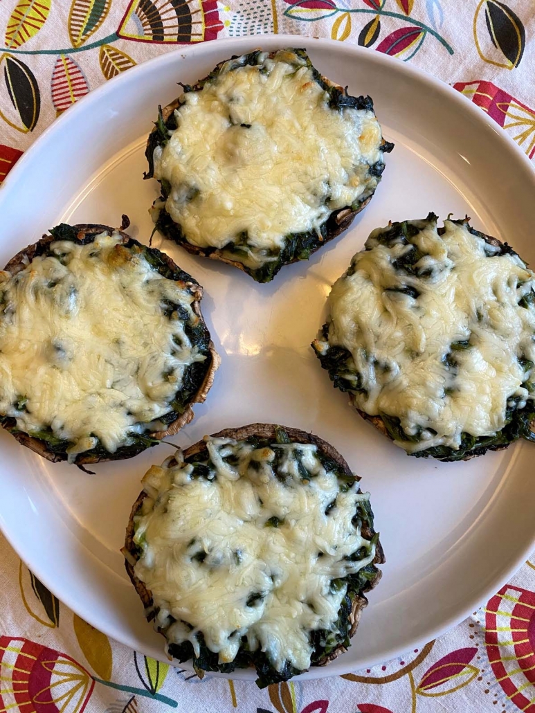 Four spinach stuffed portobello mushrooms topped with melted mozzarella cheese served on a white plate.
